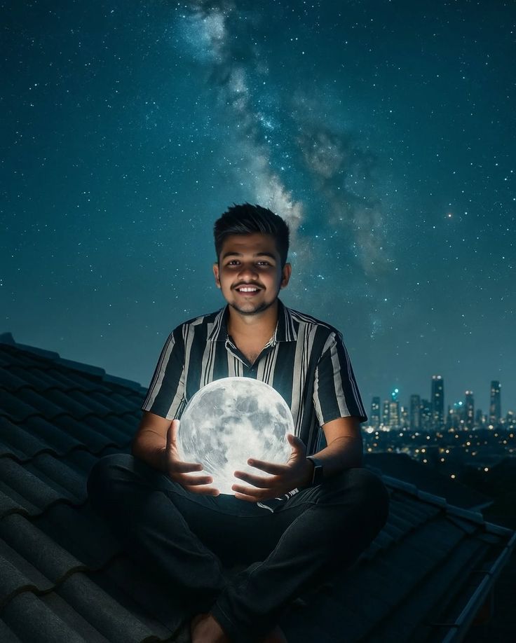 **Prompt:** > A young South Asian man sitting cross-legged on a rooftop at night, smiling and holding a bright glowing full moon lamp in his hands. The background features a starry night sky with a vibrant Milky Way galaxy and distant blurred city lights. Cinematic lighting, magical mood, high resolution, 8k, photorealistic. >  >